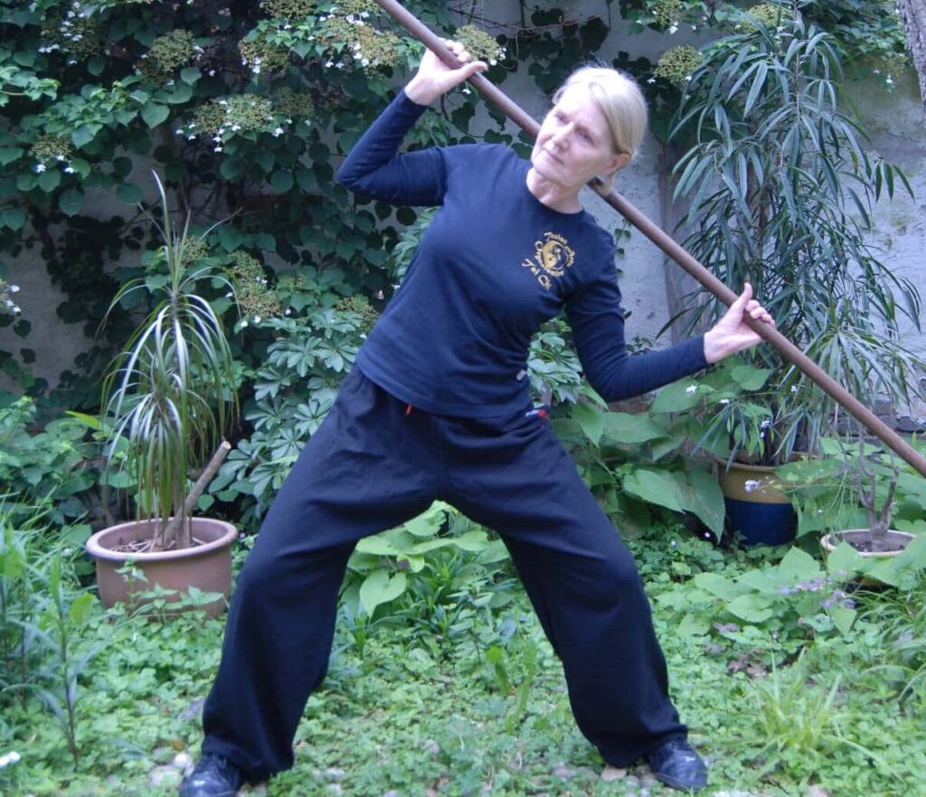 A woman practicing Chinese Yoga with a stick in her garden to achieve shoulder pain relief